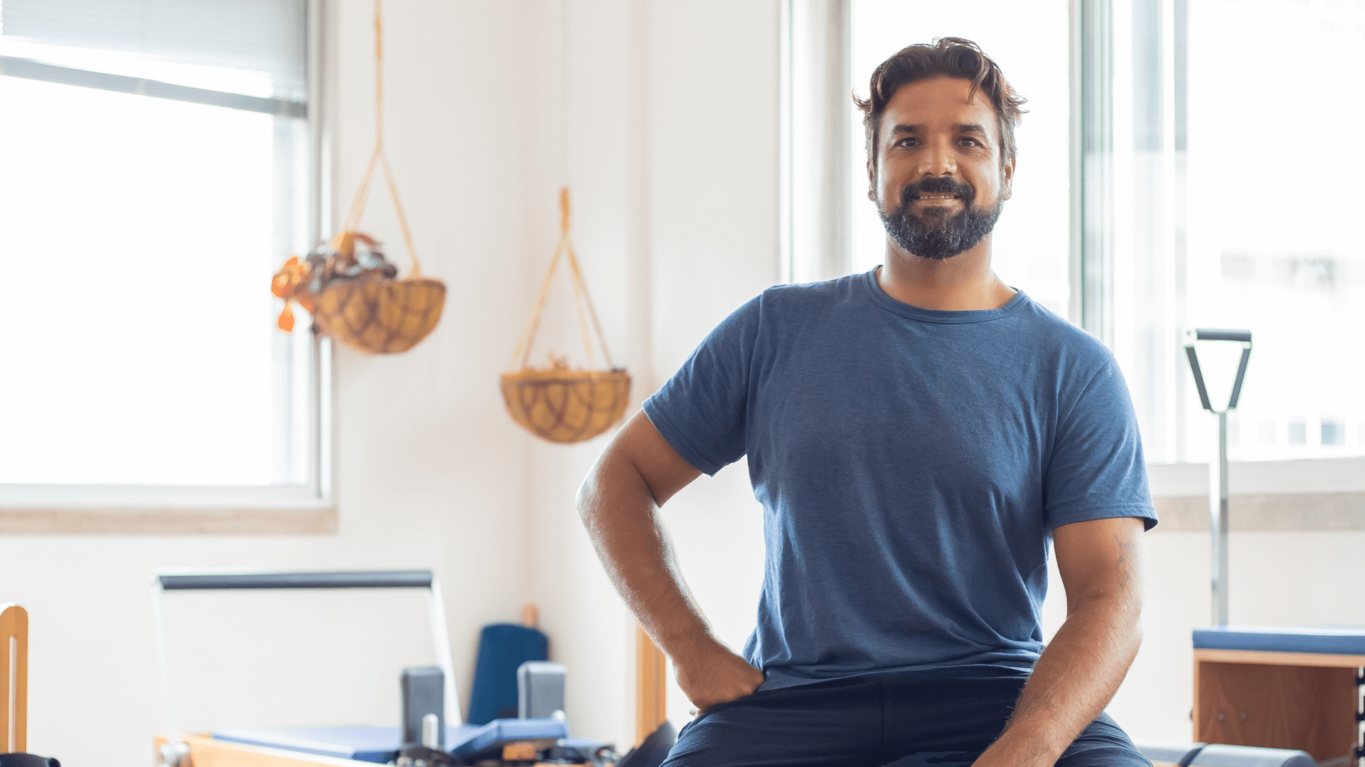 A bearded man seated in a chair, one leg is bent and the other, a prosthetic, is outstretched. He is smiling at the camera