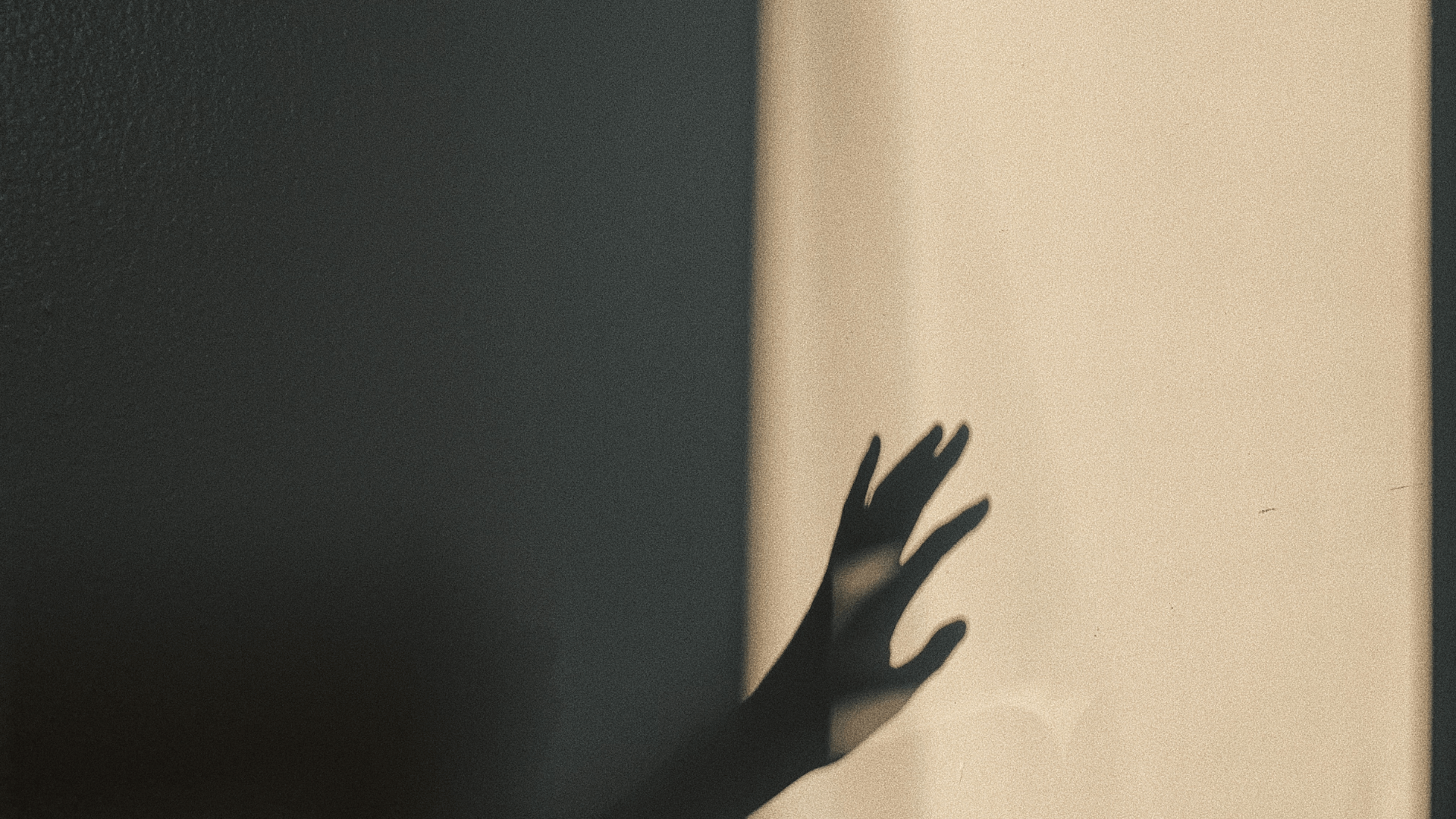 A hand in silhouette reaching out and gently touching a pane of glass